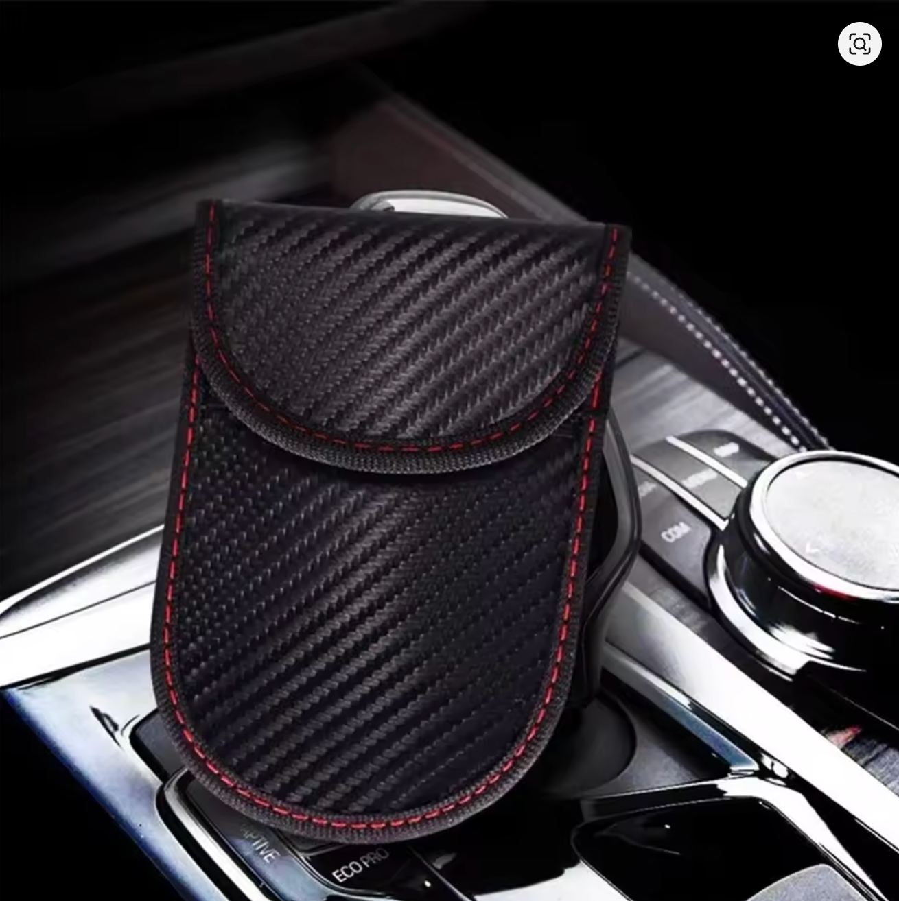 Black carbon fiber patterned signal blocking Faraday car key pouch on a gear shift on a car dashboard.