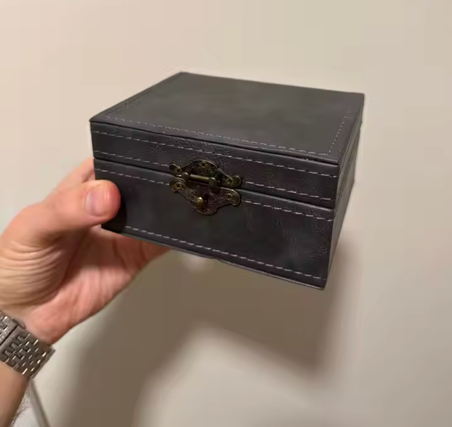 Hand holding a small black signal locking faraday box used to prevent relay theft by blocking key signals with a clasp against a plain background