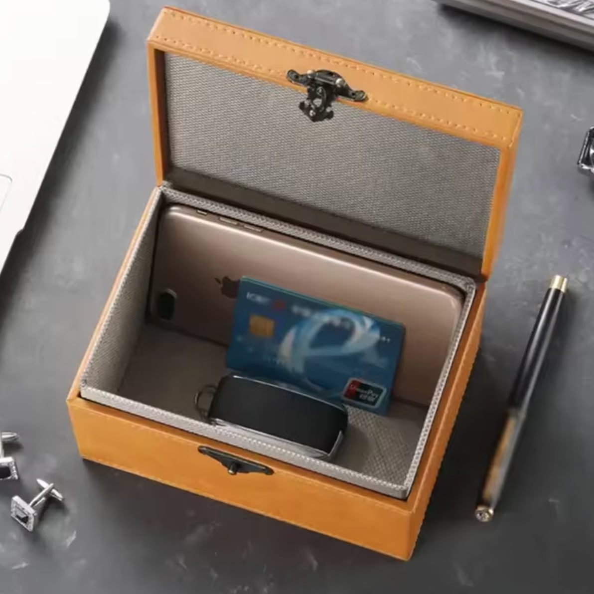 Brown signal blocking Faraday boxes for car keys to prevent keyless car theft with a card and car key fob inside on a dark surface.